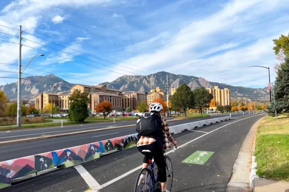 Bike lane in Boulder, Colorado with tall concrete barrier separating it from vehicle lanes and one cyclist passing by.